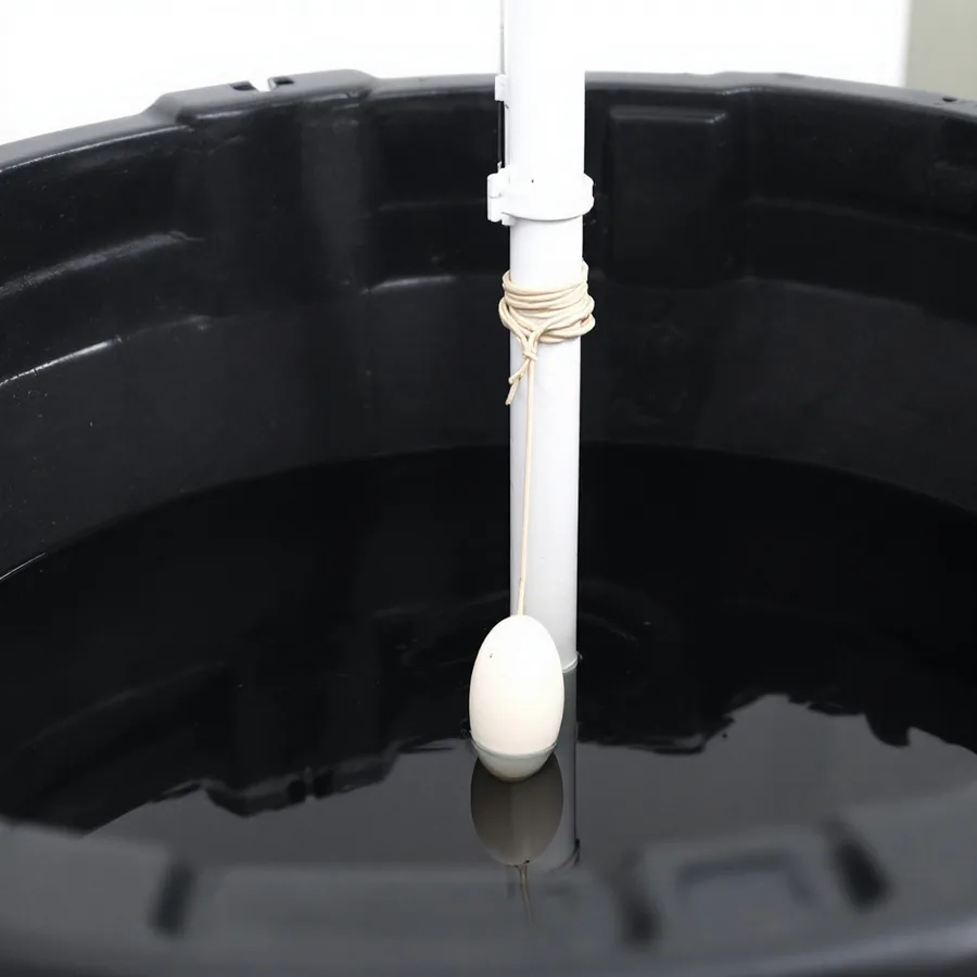 Inside a black plastic basin, a small oval float on a cord that has wrapped around the vertical discharge pipe, leaving the float hanging at the water surface unable to swing